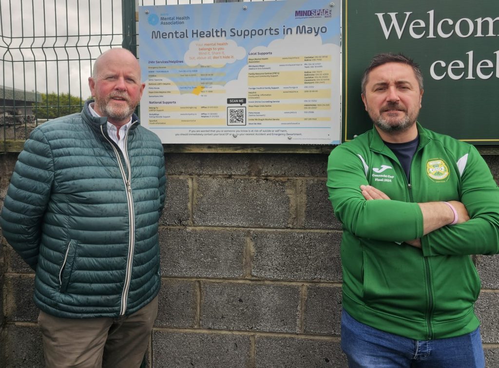 James Murray Castlebar Rotary Club and Joe  McDonald Chairman of Castlebar Celtic with the "Mayo Mental Health association " support board for sports clubs, located at the entrance to Celtic Park.